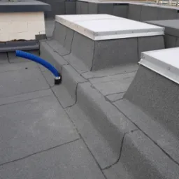 Wykończony dach pokryty papą termozgrzewalną z świetlikami dachowymi i niebieskim przewodem wentylacyjnym w Poznaniu, widok z góry.