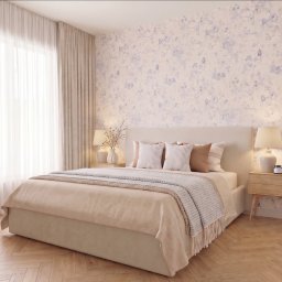 MJ Home Staging - Jasna sypialnia z łóżkiem, drewnianą podłogą w jodełkę i ścianą w kwiaty. Beżowe zasłony w oknie, lampki nocne i stoliki po bokach łóżka.