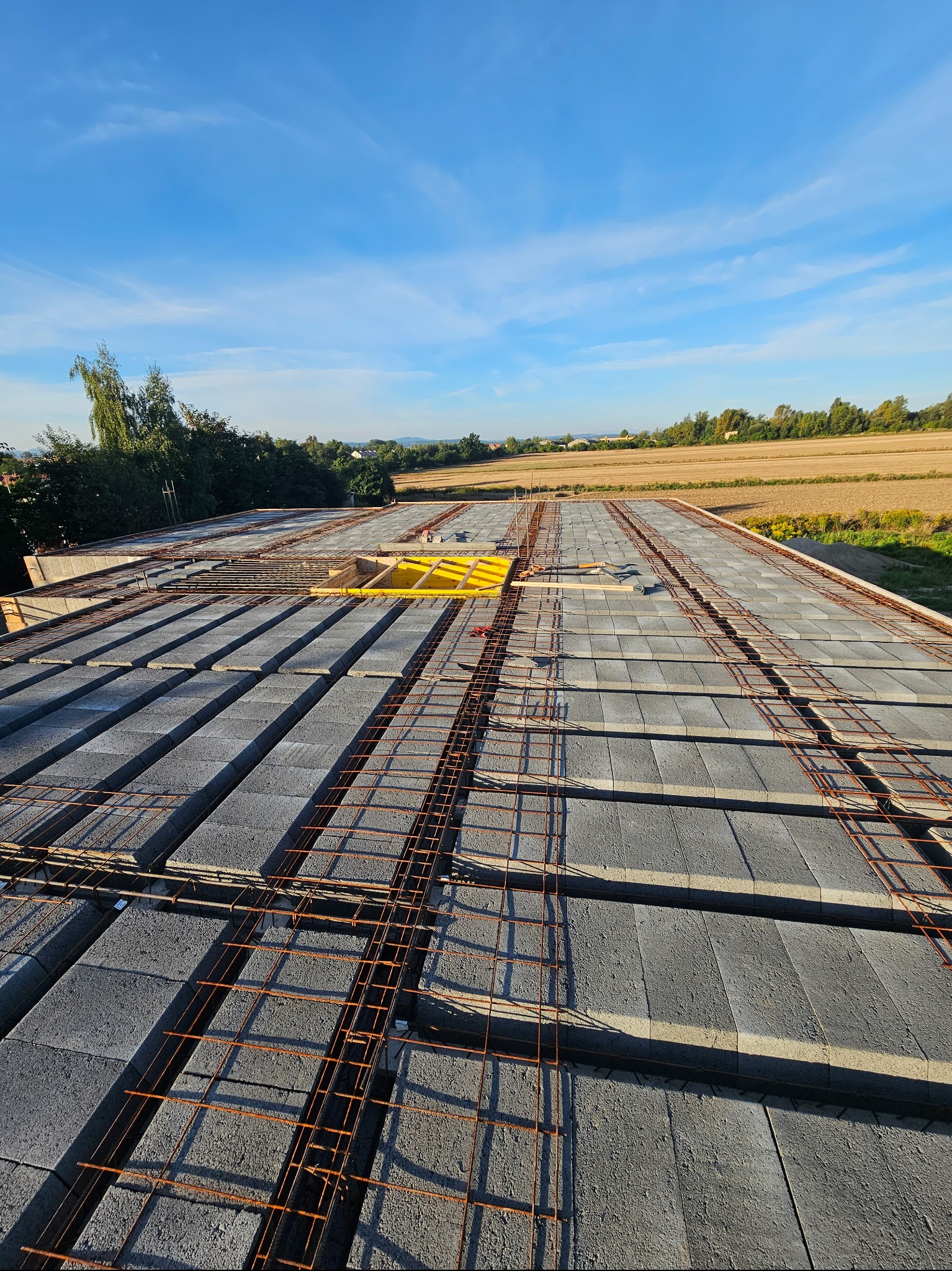 Budowa stropu Teriva z żelbetonowym wieńcem i zbrojeniem w Strzegomiu, widok z góry na konstrukcję przed zalaniem betonem, pola uprawne w tle.