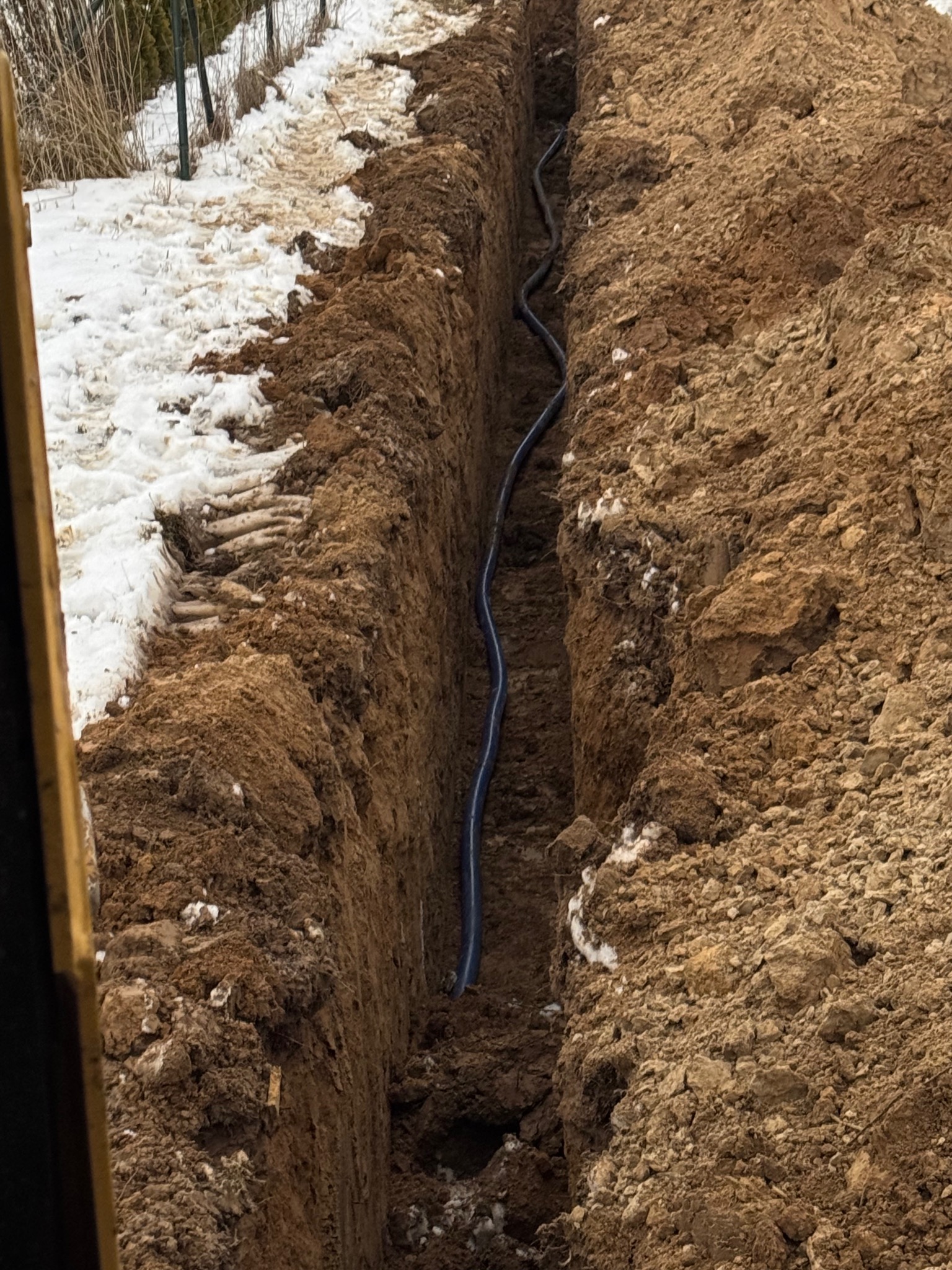 Wykopany rów z ułożoną rurą w ziemi w Krasienin-Kolonii, częściowo pokryty śniegiem, widok z góry.