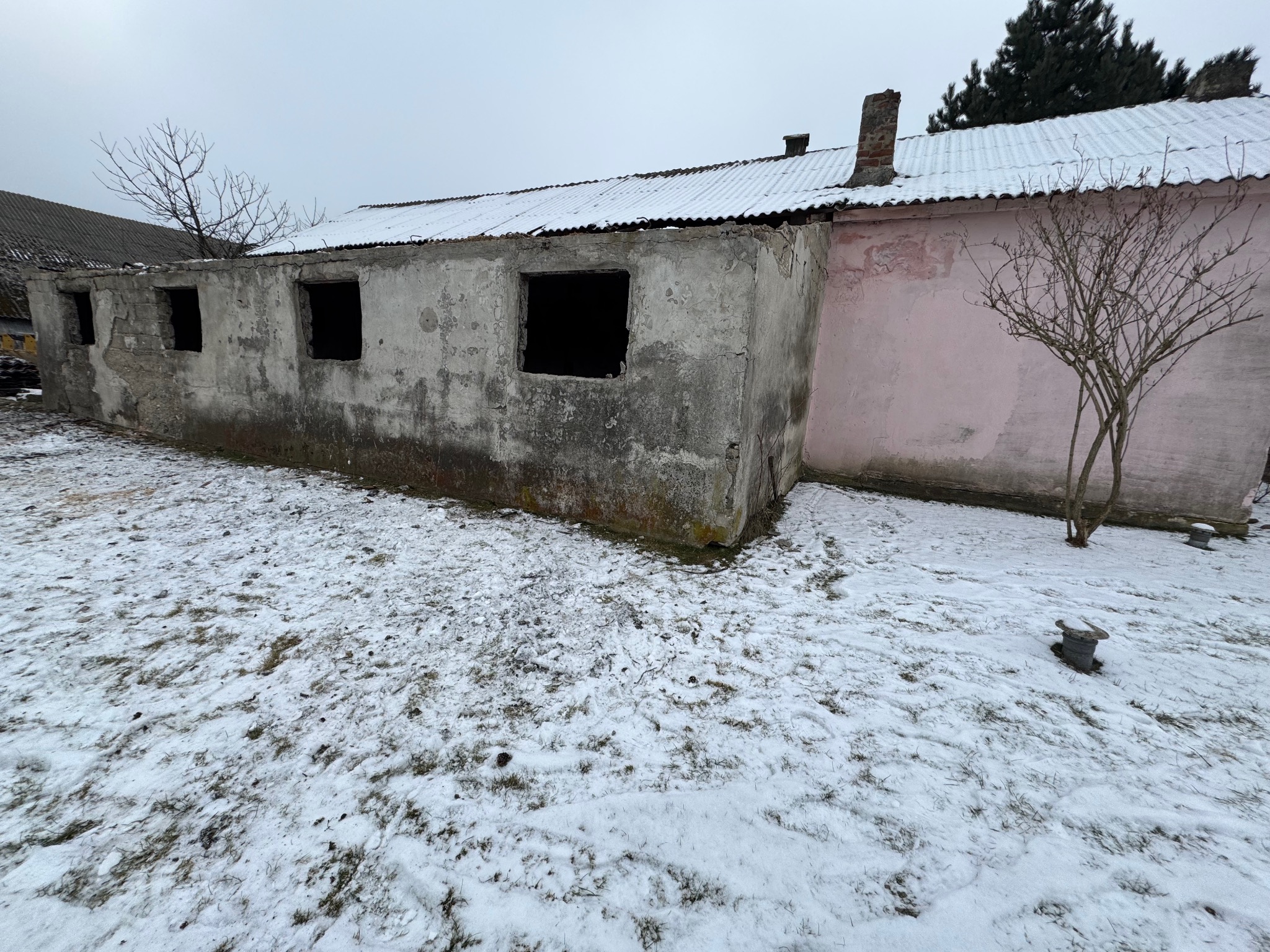 Niedokończony budynek z pustymi otworami okiennymi, częściowo otynkowany na różowo, pokryty śniegiem, widoczny w zimowym krajobrazie.