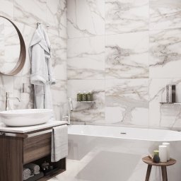 Viktor Nenakhov - Nowoczesna łazienka z białymi płytkami imitującymi marmur, owalną umywalką na drewnianej szafce, białą wanną wolnostojącą i okrągłym lustrem z drewnianą ramą. Na ścianie zawieszony biały szlafrok...