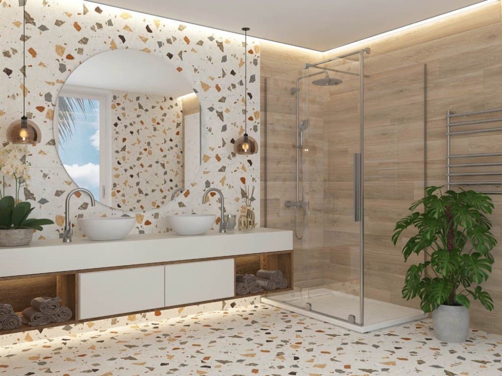 Nowoczesna łazienka z podwójną umywalką nablatową, okrągłym lustrem, kabiną prysznicową ze szklanymi drzwiami i mozaikową okładziną ścian oraz podłogi.