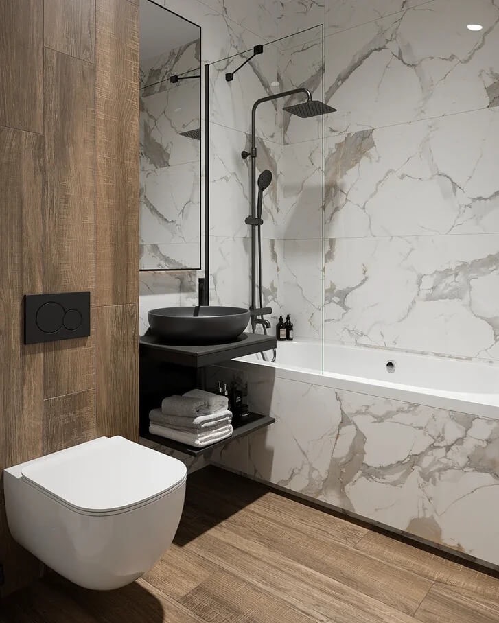 Nowoczesna łazienka z marmurowymi płytkami, czarną armaturą i drewnopodobną podłogą, widok na umywalkę nablatową, toaletę podwieszaną i wannę za szklanym panelem.