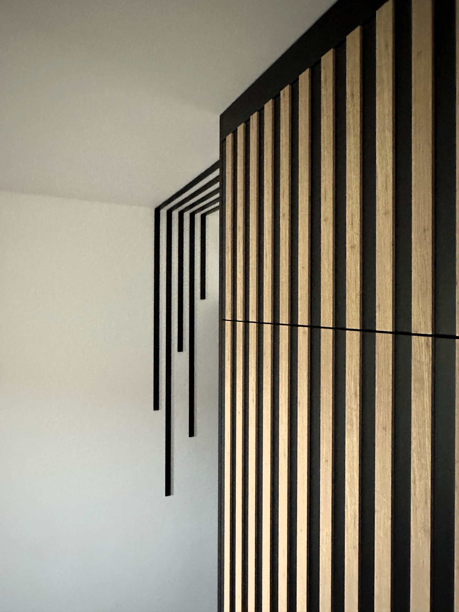 Minimalistyczna szafa z lamelami z jasnego drewna i czarnymi elementami dekoracyjnymi na ścianie.