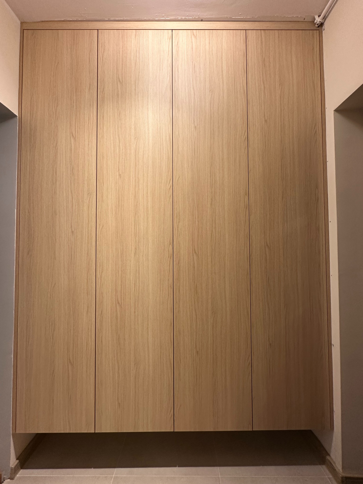 Pełna zabudowa wnęki z czterema frontami z jasnego drewna, minimalistyczny design, widoczne łączenia paneli.