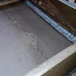 Metalowa konstrukcja spawana, widoczne spoiny wewnątrz ramy, z otworami wzdłuż jednej krawędzi.