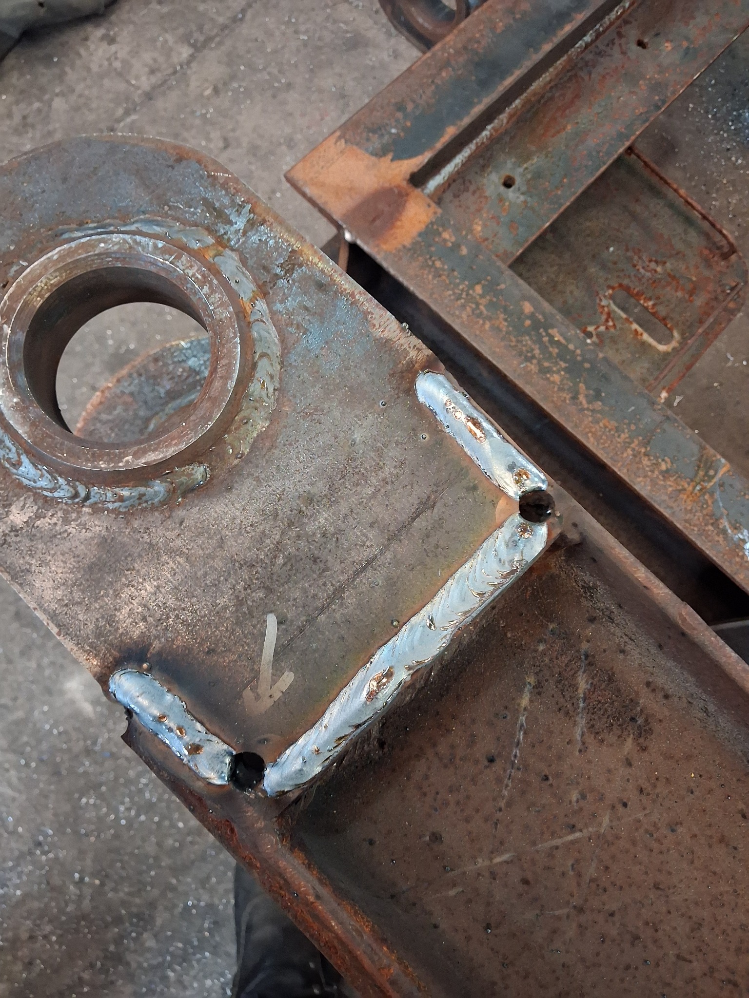 Fragment konstrukcji stalowej z widocznymi spawami, otworem i śladami rdzy, ukazujący detale łączenia elementów.