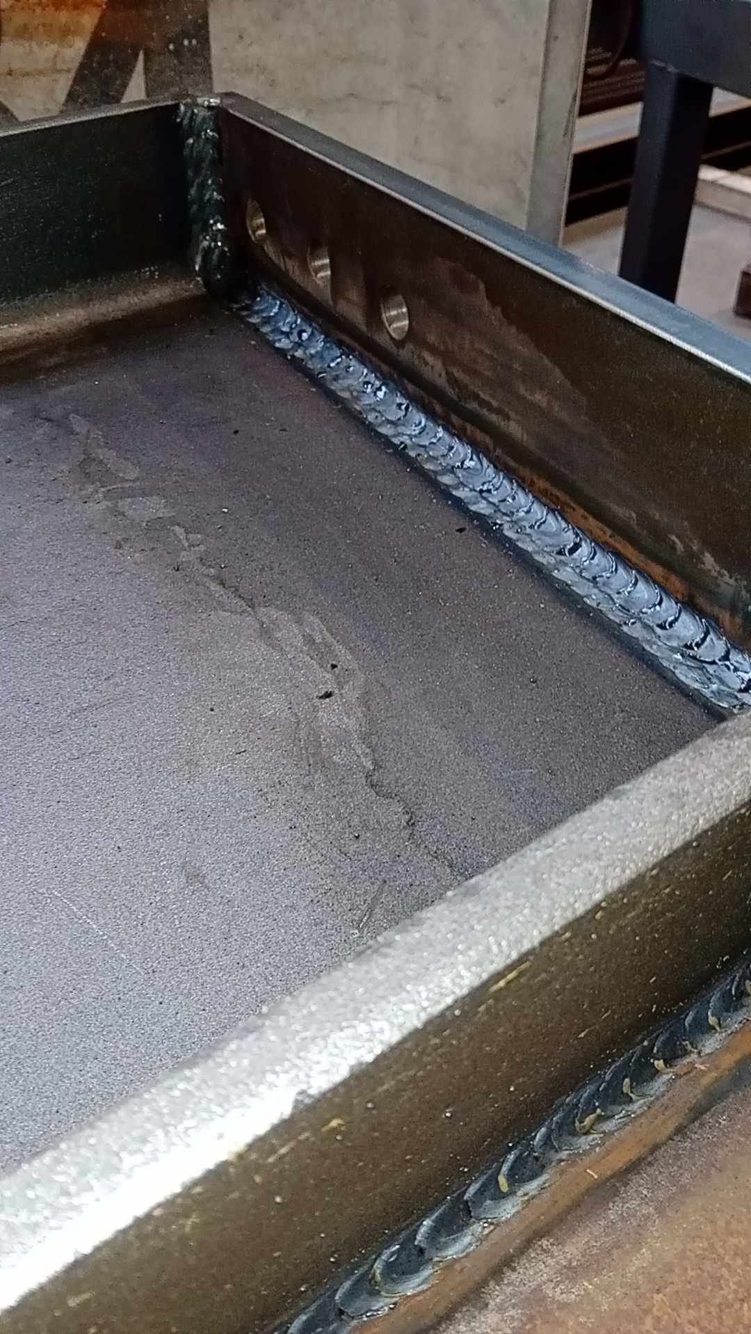 Metalowa konstrukcja spawana, widoczne spoiny wewnątrz ramy, z otworami wzdłuż jednej krawędzi.