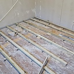 Usługi Remontowo Budowlane - Przygotowanie podłoża pod parkiet: drewniane legary ułożone na starej podłodze, widoczne ślady po gładzi na ścianach.