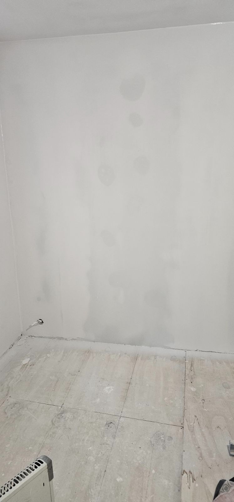 Świeżo zagruntowana ściana z widocznymi śladami po szpachlowaniu, surowa podłoga z płyt OSB, grzejnik w rogu pomieszczenia.