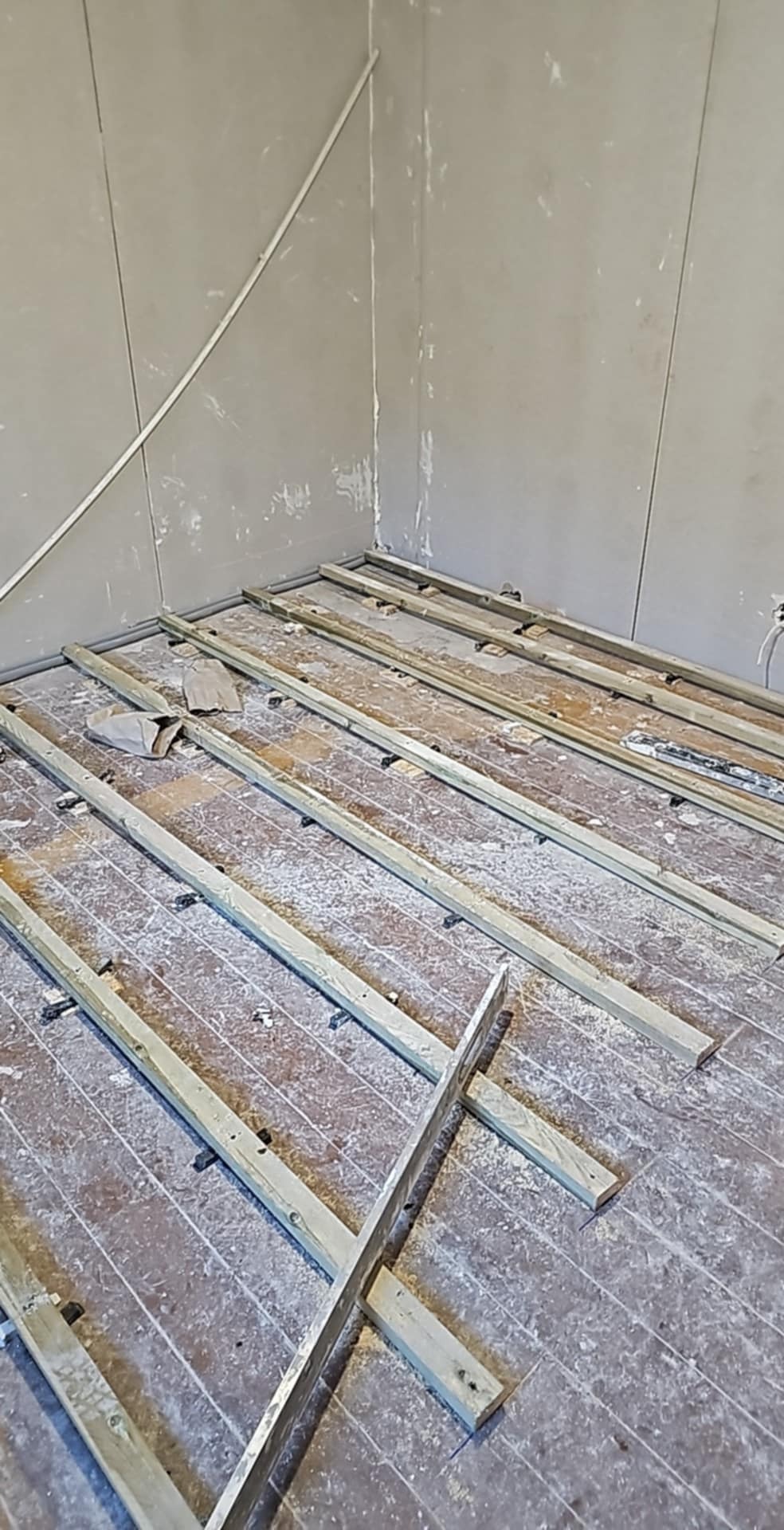 Przygotowanie podłoża pod parkiet: drewniane legary ułożone na starej podłodze, widoczne ślady po gładzi na ścianach.