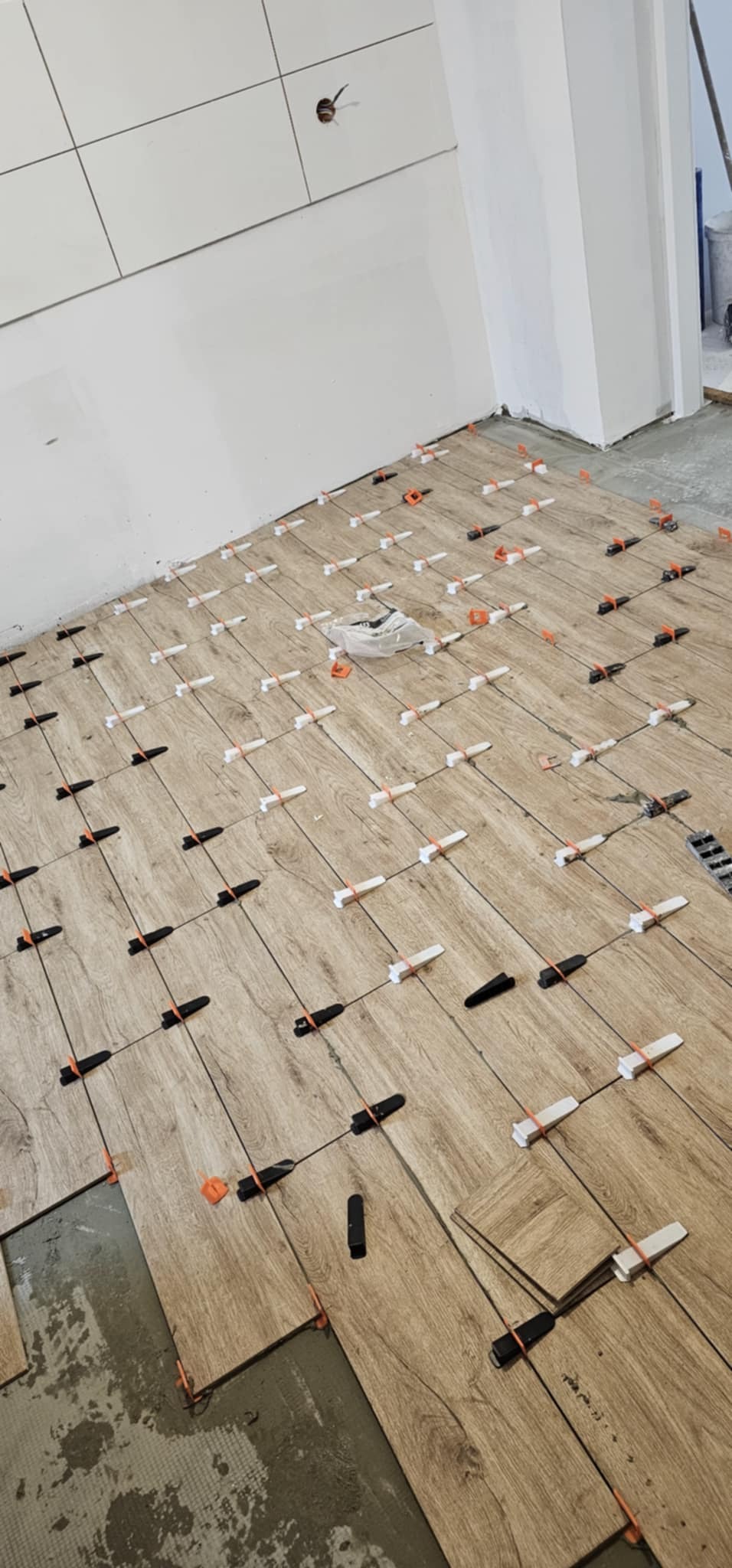 Układanie płytek podłogowych imitujących drewno, z zastosowaniem systemu poziomowania płytek (klipsy i kliny) w trakcie prac.