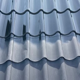 MalProf Renowacje Malowanie Dachów i Elewacji - Błyszcząca, grafitowa dachówka ceramiczna w zbliżeniu, z widocznymi mocowaniami i refleksami światła, ukazująca regularny wzór i gładką powierzchnię.