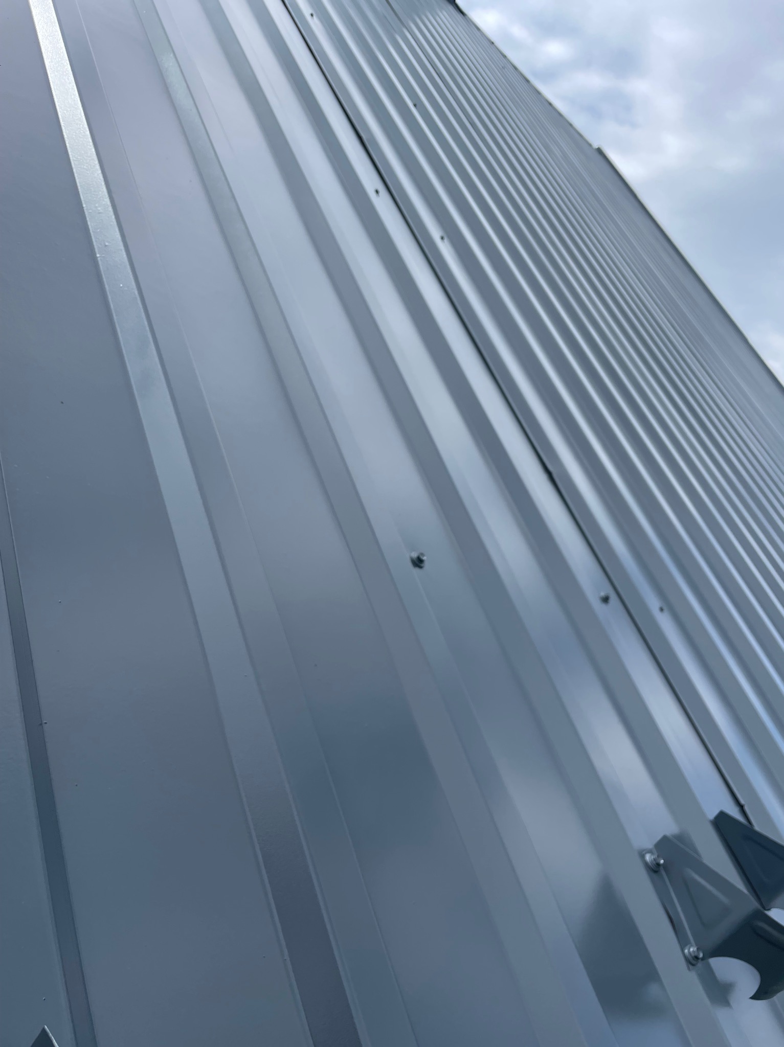 Nowo pomalowany, szary dach z blachy trapezowej, widoczny pod kątem z fragmentem orynnowania, na tle pochmurnego nieba.