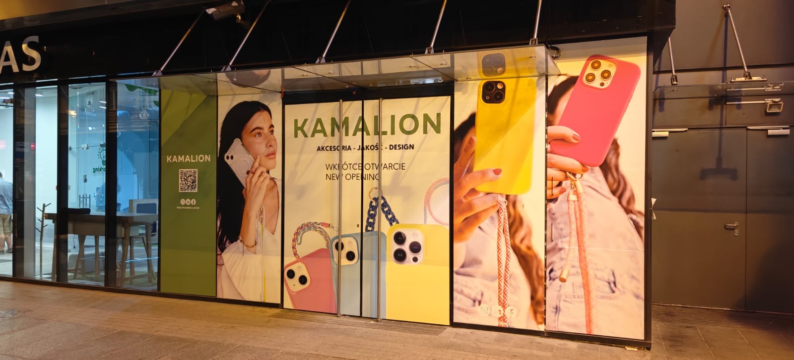 Fasada sklepu z akcesoriami do telefonów Kamalion, z dużymi plakatami reklamowymi prezentującymi etui na telefony w różnych kolorach i wzorach. W tle widoczne wnętrze sklepu.