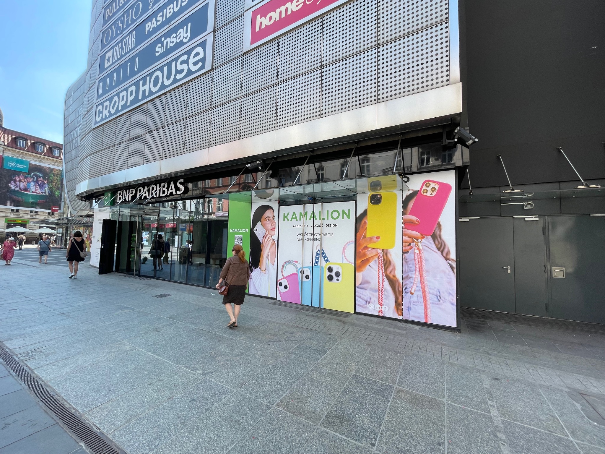 Billboard reklamowy sklepu z akcesoriami do telefonów 'Kamalion' na fasadzie budynku w centrum miasta. Widoczni przechodnie.