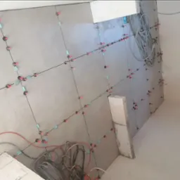 Świeżo położone szare płyty kartonowo-gipsowe na ścianie, z widocznymi systemami poziomowania płytek (klipsy i kliny), oraz zwisającymi kablami elektrycznymi.