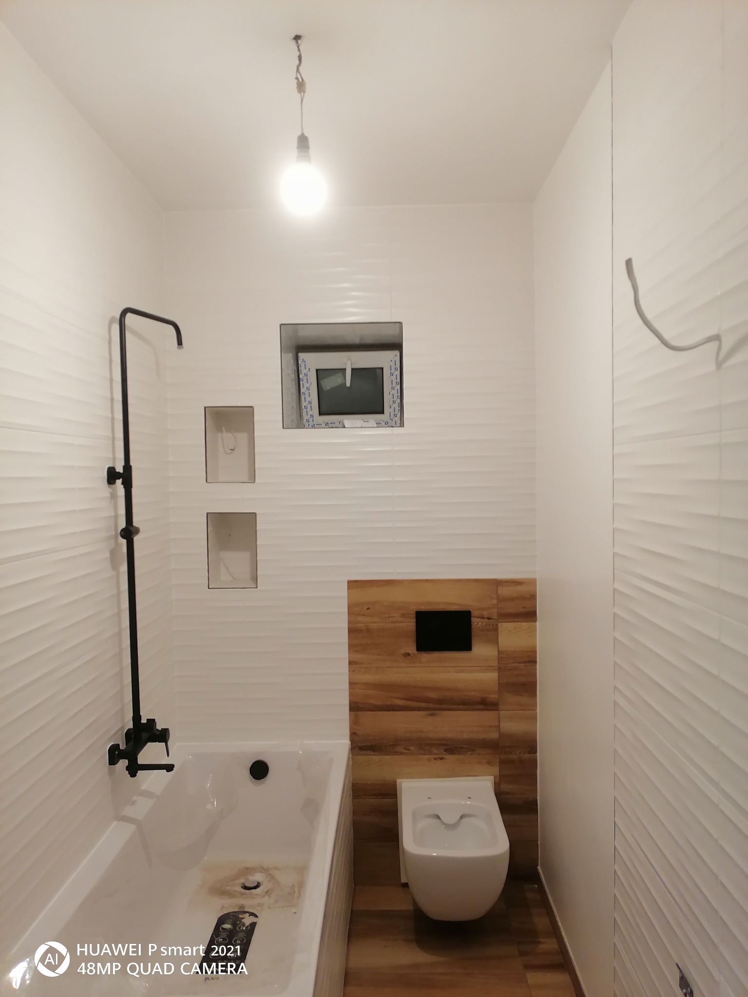 Nowoczesna łazienka z białą wanną, czarną armaturą, toaletą podwieszaną na drewnianym panelu, oświetleniem punktowym i falistymi białymi płytkami na ścianach.