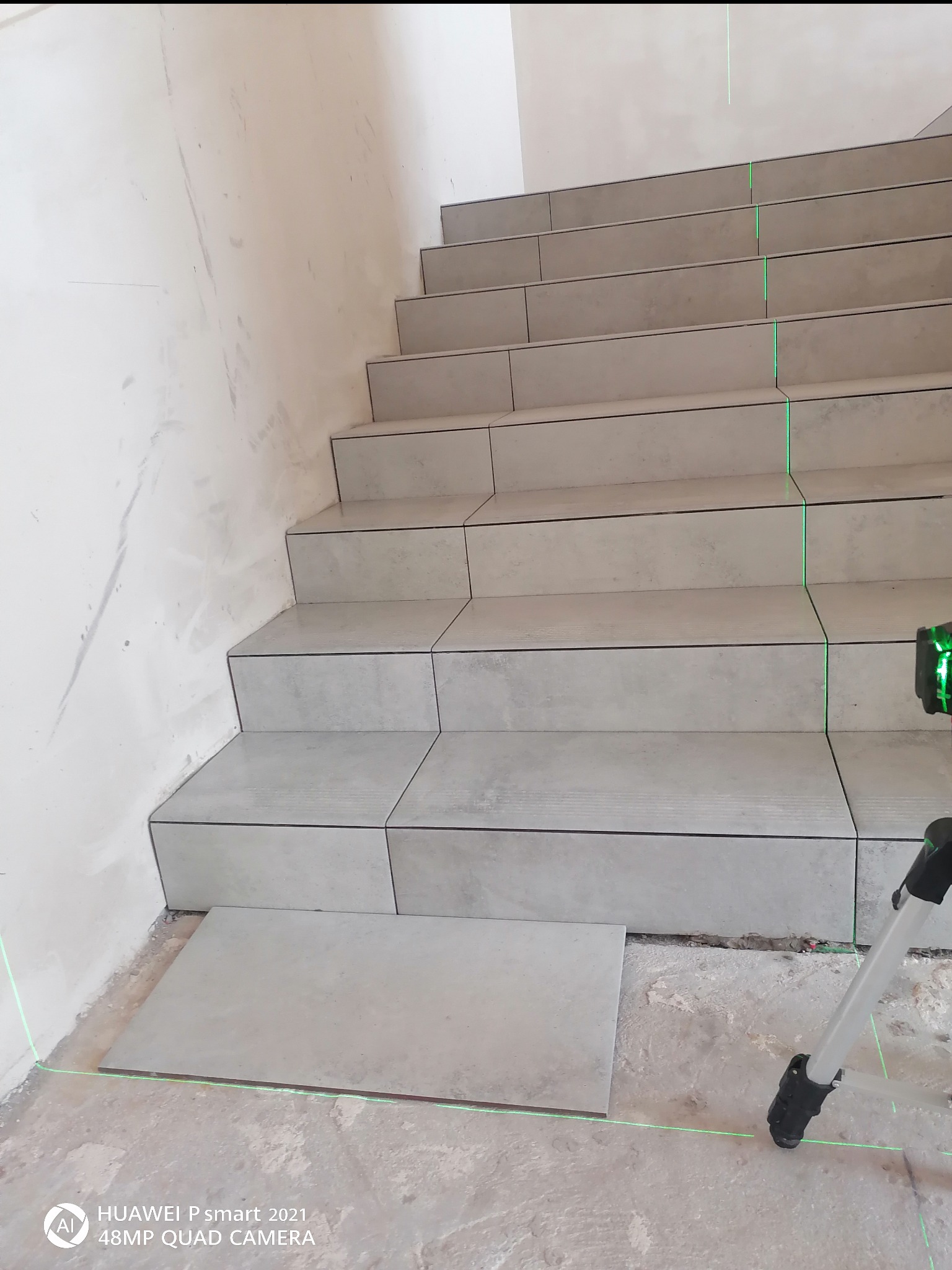 Wykończenie schodów płytkami ceramicznymi, widoczny laser krzyżowy i nieułożona płytka na podłodze.