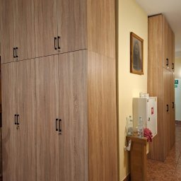 SimWood Szymon Niezgoda - Beżowe szafy wnękowe z czarnymi uchwytami, ustawione w rzędzie wzdłuż ściany. Na ścianie wisi obraz. Widoczny fragment podłogi z brązowych płytek.