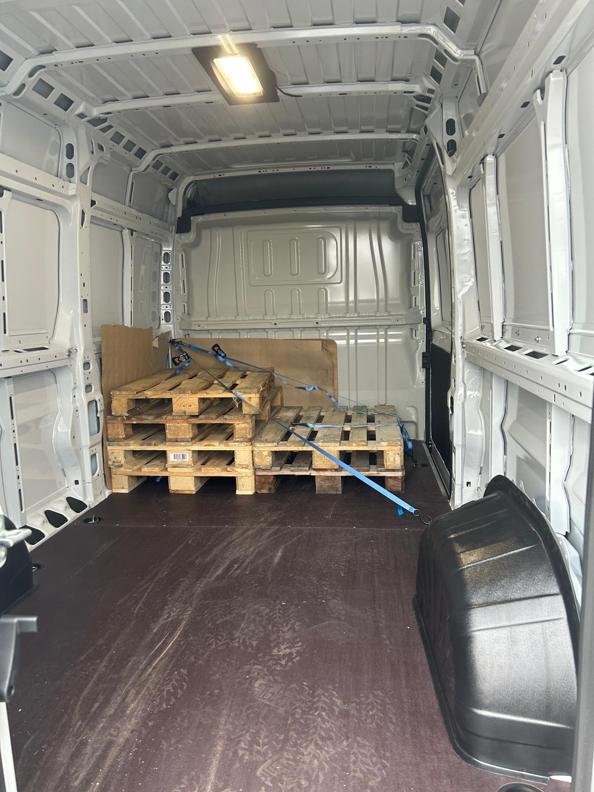 Wnętrze czystego, białego busa transportowego z paletami zabezpieczonymi niebieskimi pasami transportowymi, widoczne ślady użytkowania na podłodze.