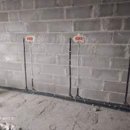 Bohdan Bohdan - Surowy mur z betonu komórkowego z widocznymi przewodami elektrycznymi w peszlach, prowadzącymi do pomarańczowych puszek instalacyjnych.