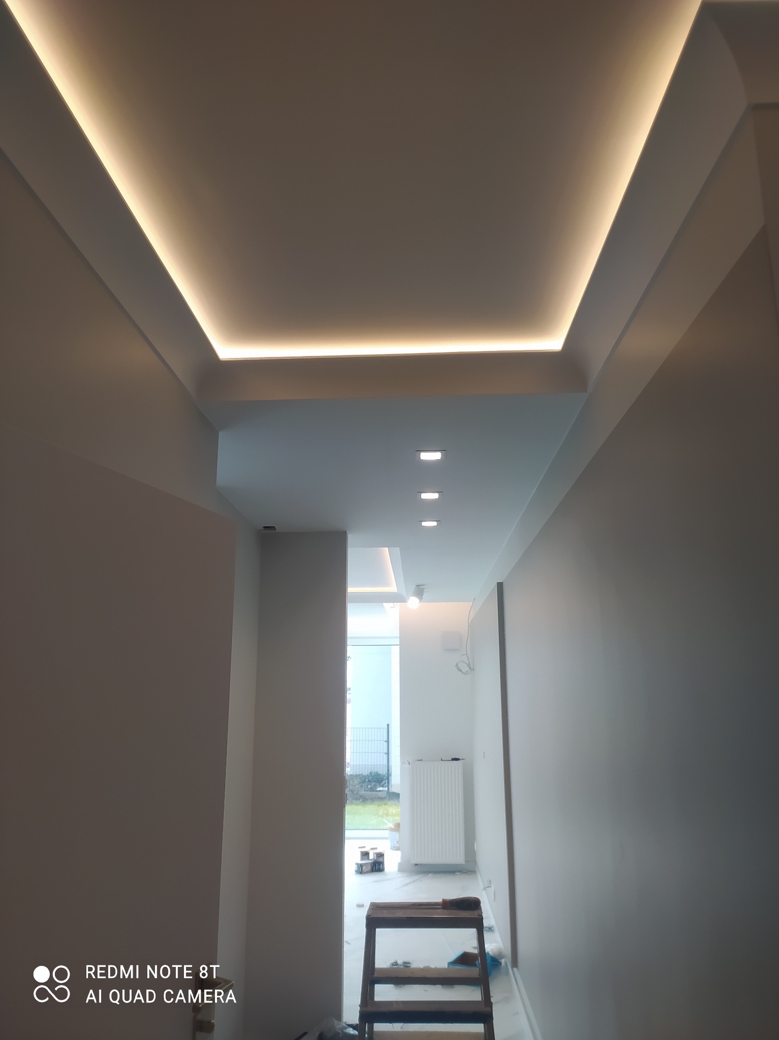 Nowoczesne oświetlenie sufitowe LED w korytarzu, listwa LED w obniżonym suficie podwieszanym, widok z dołu na drewnianą drabinę malarską.