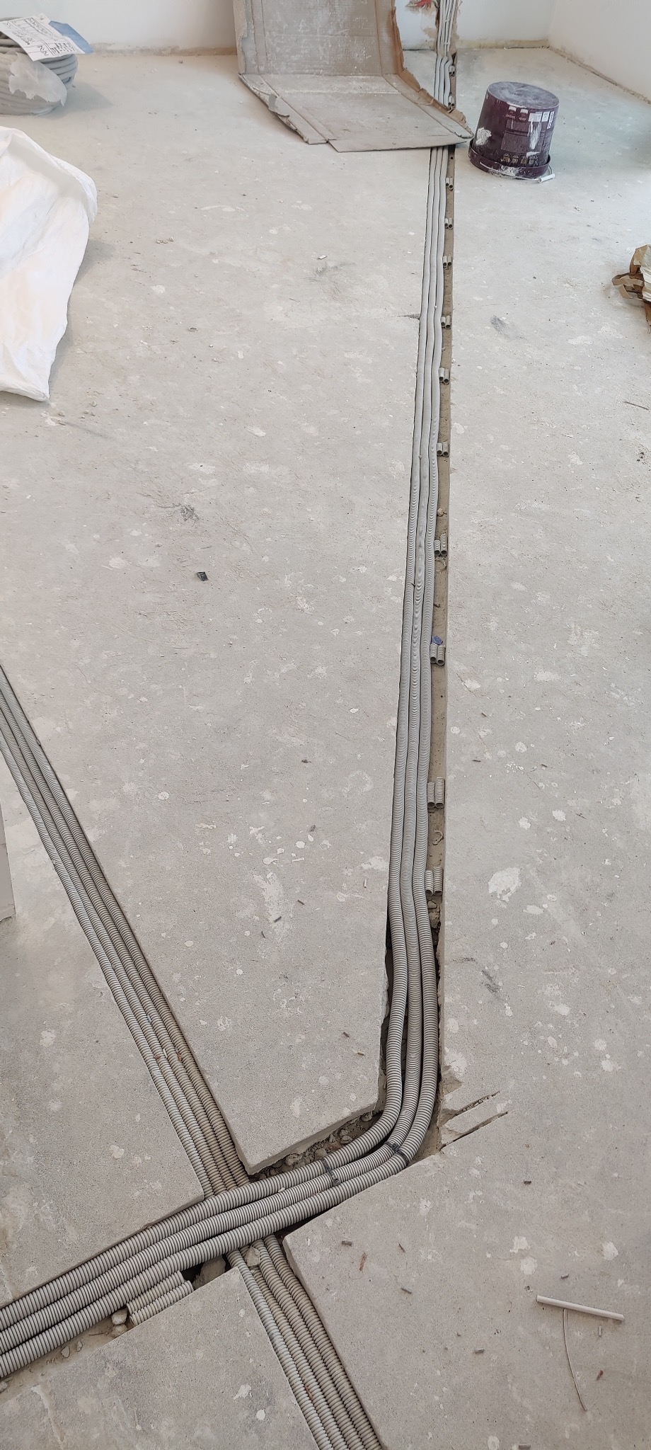 Bruzdowanie w posadzce pod kable elektryczne w peszlach, widoczne kable ułożone w wyciętych rowkach w betonie, przygotowanie do zalania wylewką.