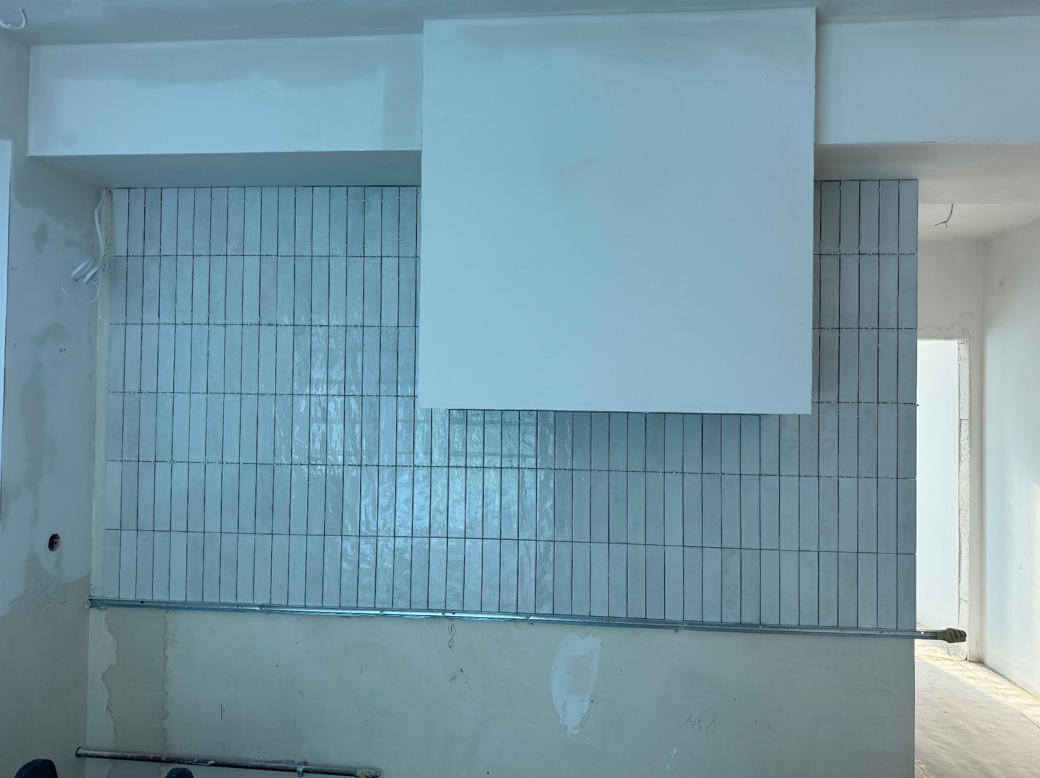 Montaż pionowych, błyszczących, szarych płytek na ścianie w trakcie prac wykończeniowych, widoczna metalowa listwa montażowa i surowa ściana w dolnej części.