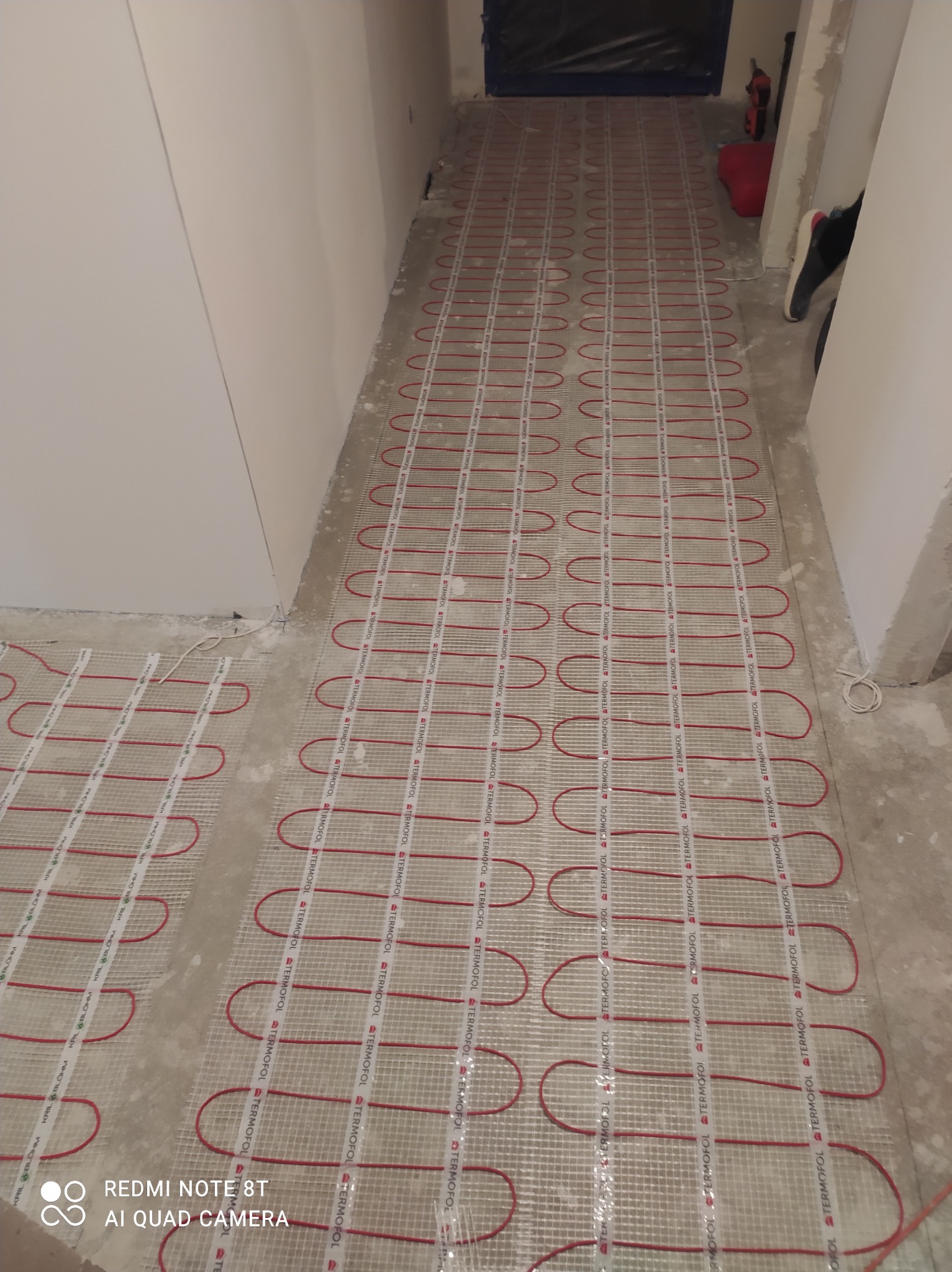 Rozłożona mata grzewcza z czerwonymi przewodami na siatce, przygotowana do zalania wylewką w trakcie prac wykończeniowych w pomieszczeniu.