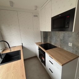 GRAB-TECH Aleksandra Grabowska - Nowoczesna kuchnia w jasnych barwach z drewnianym blatem, czarnym zlewem i baterią, oraz zabudowaną kuchenką mikrofalową Amica.