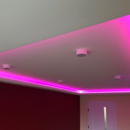 GRAB-TECH Aleksandra Grabowska - Sufit podwieszany z oświetleniem LED w kolorze różowym, z widocznymi punktowymi lampami, na tle bordowej ściany i białych drzwi.