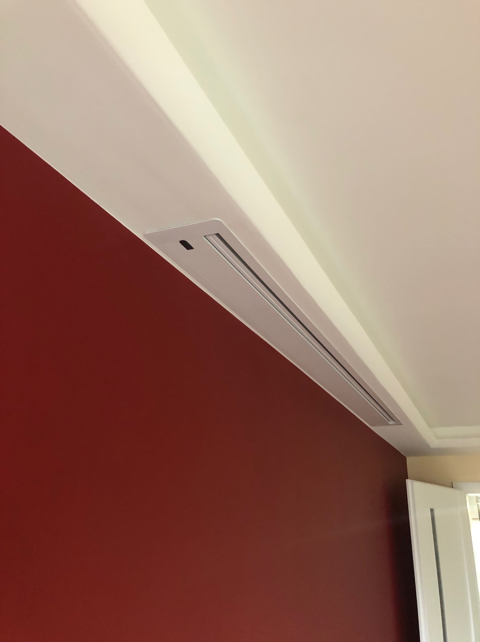 Szczegół wykończenia wnętrza: Czerwona ściana kontrastuje z białym sufitem, w którym zamontowany jest liniowy nawiewnik klimatyzacji.