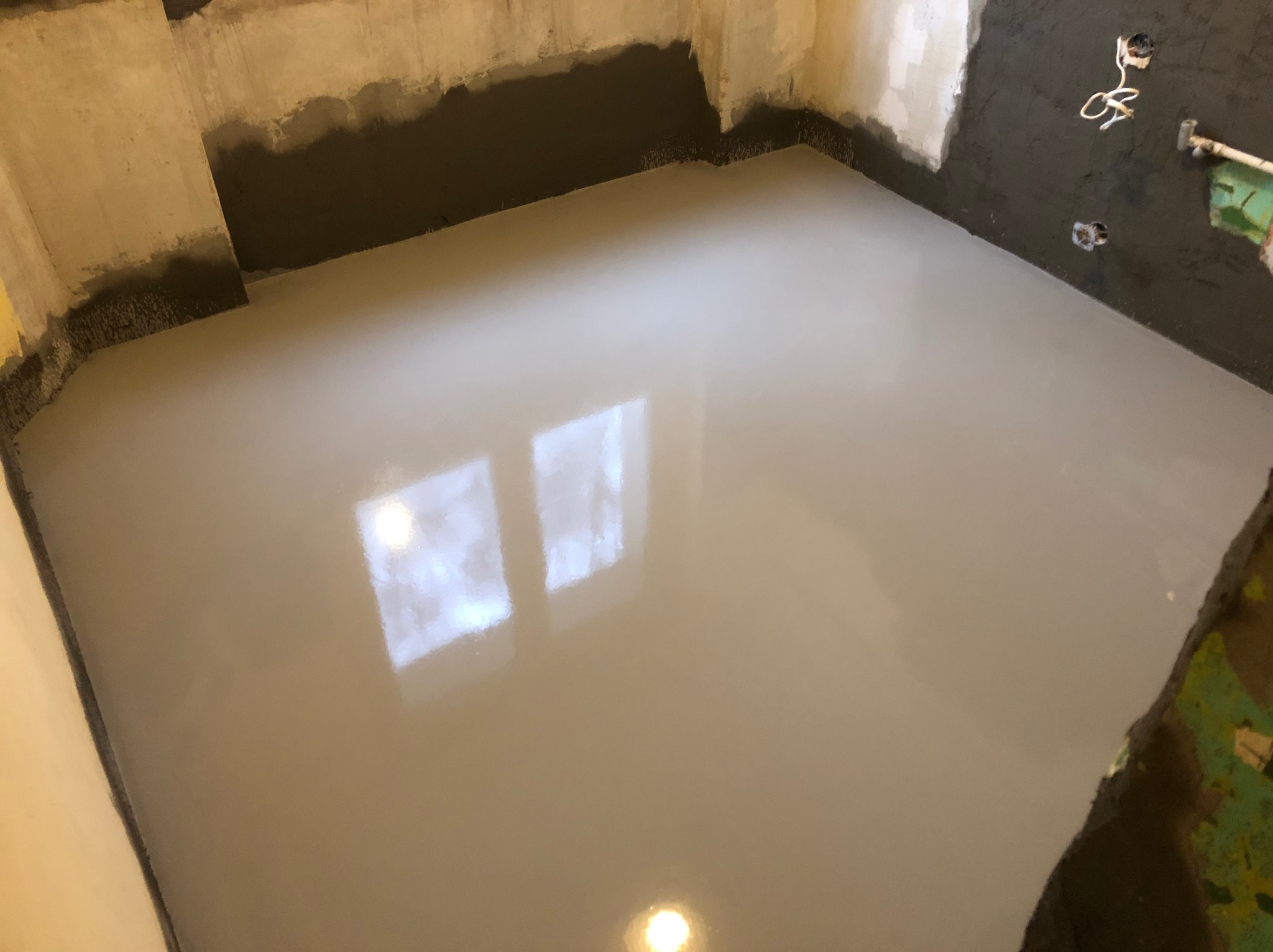 Wylany samopoziomujący podkład podłogowy w trakcie schnięcia, widoczne ślady po pracach na ścianach, przygotowane gniazdka elektryczne.