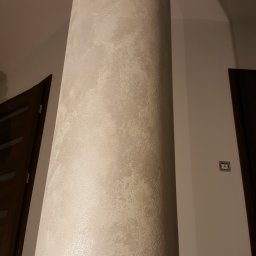 WB Master Wojciech Boruch - Dekoracyjny filar w jasnych odcieniach beżu z efektem strukturalnym, widoczny fragment ściany i drzwi z ciemnego drewna. Całość w ciepłym oświetleniu.