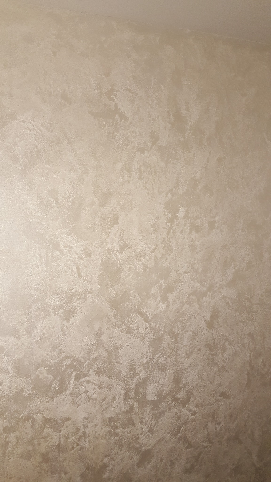Ściana pokryta dekoracyjną, beżową gładzią w stylu weneckim, z subtelnymi refleksami światła, ukazująca fakturę i wzór na całej powierzchni ściany.