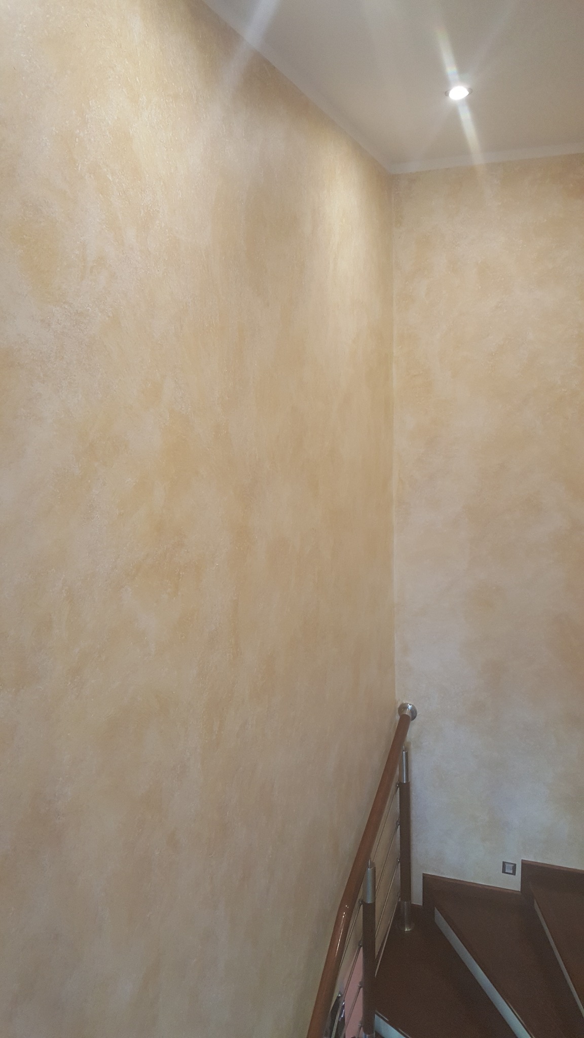 Ściana z efektem dekoracyjnym w odcieniach beżu i brązu, widok z dołu schodów z drewnianymi stopniami i metalowo-drewnianą balustradą w nowoczesnym wnętrzu.