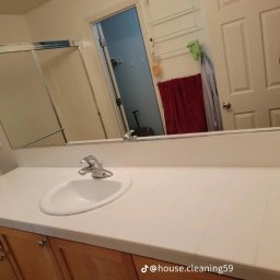 BioCleanMaster - Umywalka z białym blatem w łazience, widoczne odbicie w lustrze z suszącymi się ręcznikami i otwartymi drzwiami prysznica.