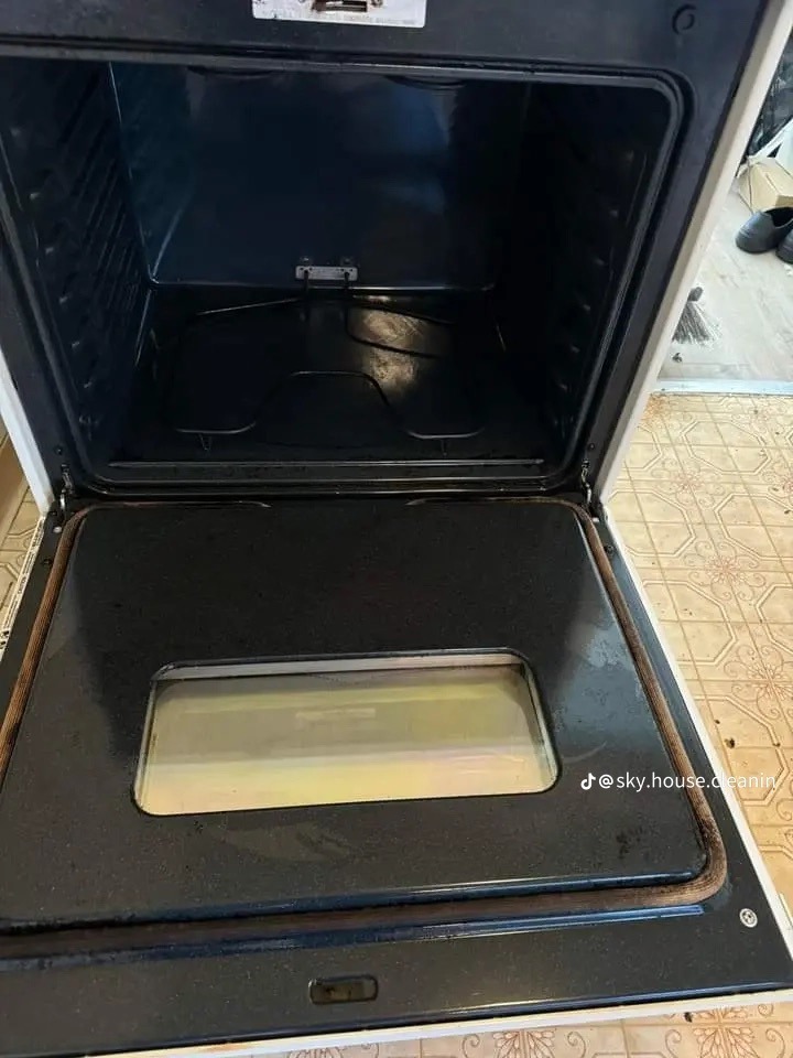 Wnętrze brudnego piekarnika z otwartymi drzwiczkami przed czyszczeniem, widoczne przypalone resztki jedzenia na dnie i ściankach.