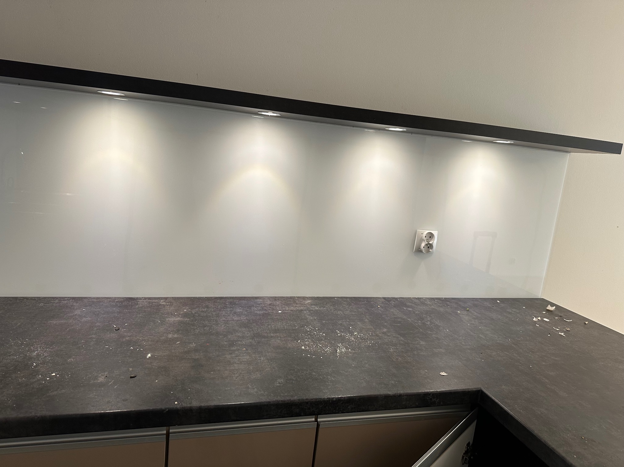 Brudny blat kuchenny z pozostałościami po remoncie, podświetlany paskiem LED. Widoczne gniazdko elektryczne i fragment szafek kuchennych.