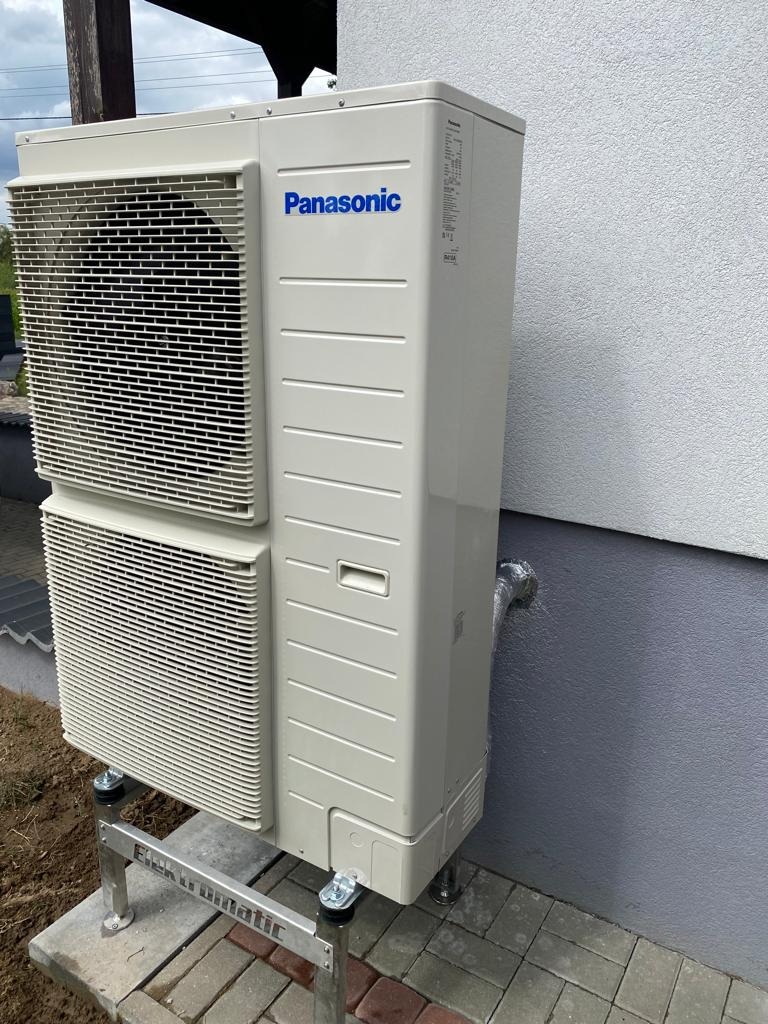 Zewnętrzna jednostka klimatyzacji Panasonic zamontowana na metalowej konstrukcji Elektromatic przy ścianie budynku w Brodnicy, z widocznym przewodem odprowadzającym skropliny.