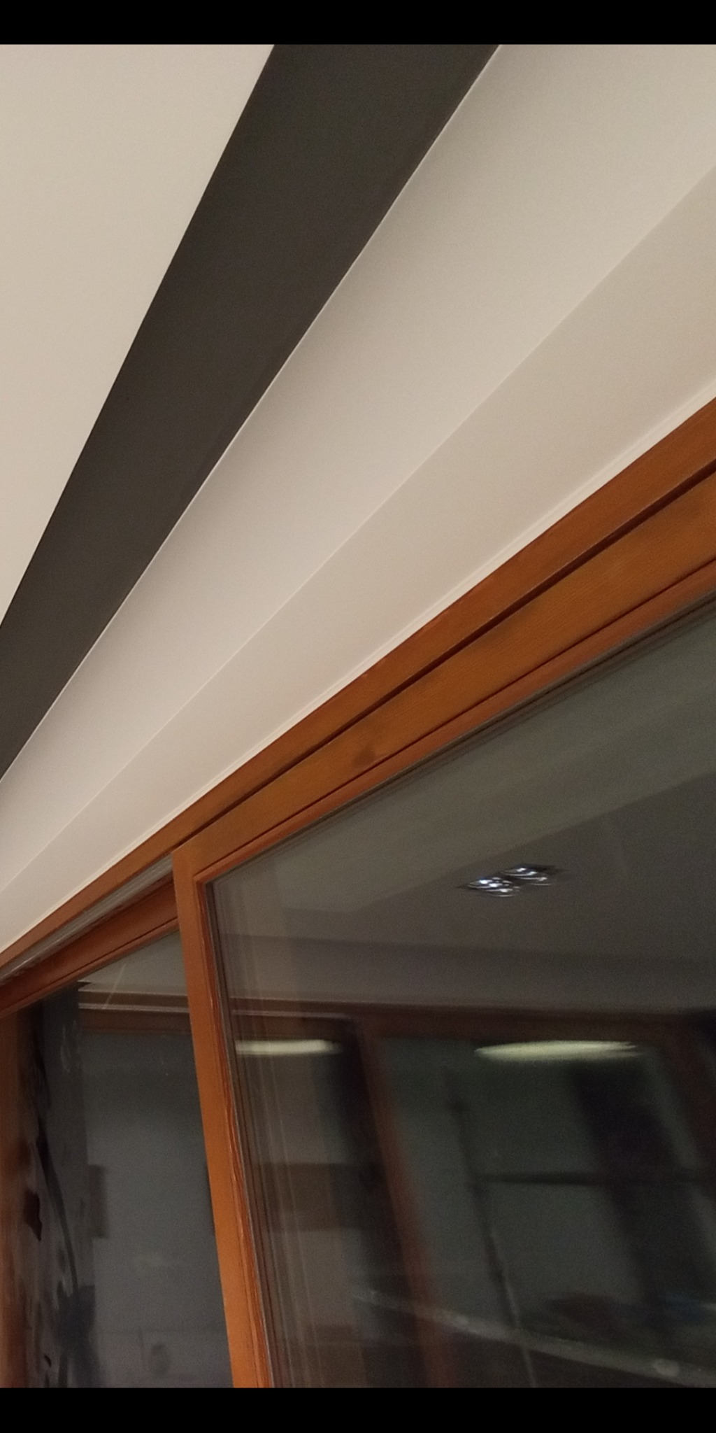 Pomieszczenie po remoncie: biało-szare pasy na suficie, drewniane wykończenie okna, widoczne odbicie oświetlenia w szybie.