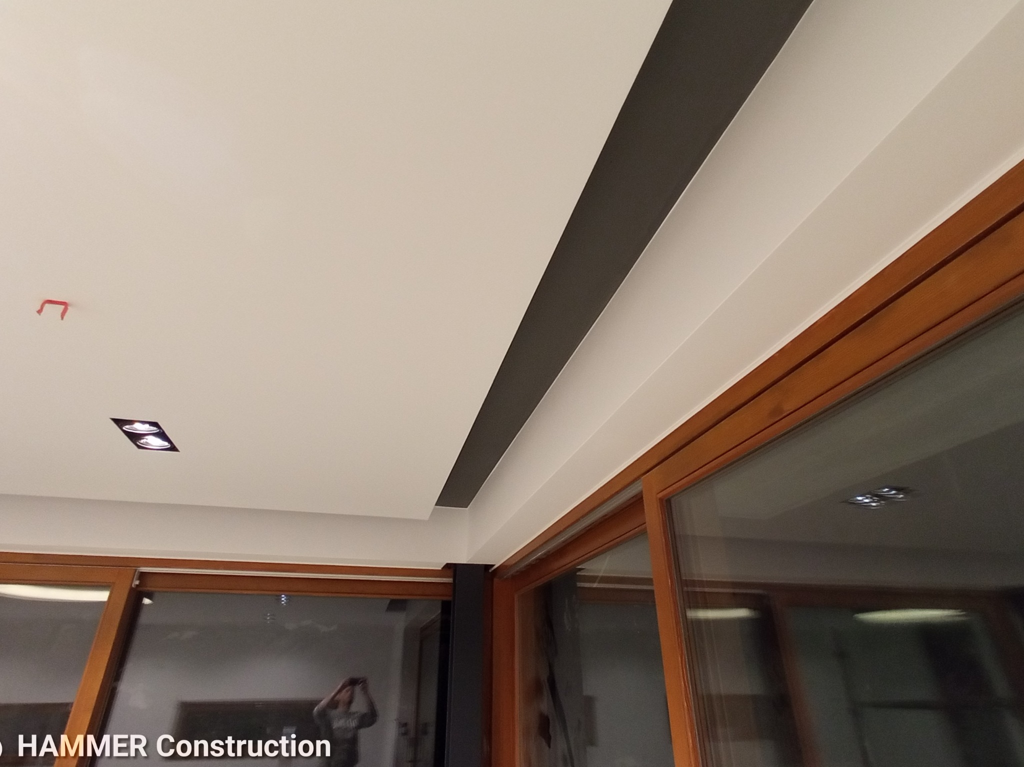 Fragment wnętrza z pomalowanym sufitem, z widoczną wnęką pomalowaną na szaro, oświetleniem punktowym i drewnianą ramą okienną.