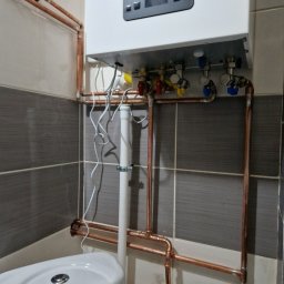 TK-SERWIS Kamil Tymiak - Nowoczesny piec gazowy Termet z miedzianą instalacją w łazience, Wałbrzych. Widoczne zawory, rury i biała obudowa pieca na tle szaro-białych płytek.