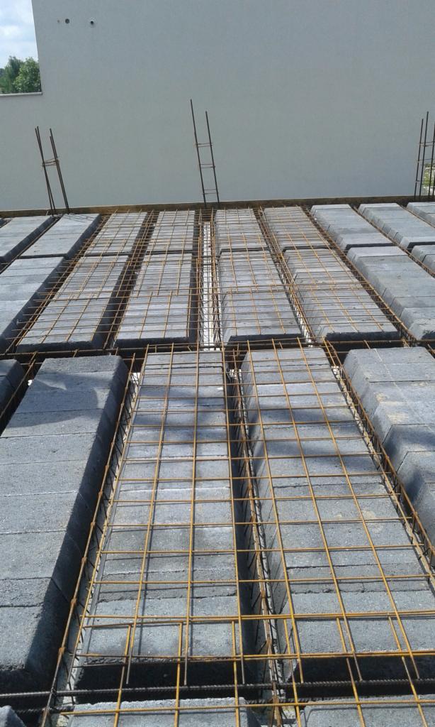 Szare bloczki betonowe ułożone na stropie, wzmocnione siatką zbrojeniową, widok z góry na budowę domu.