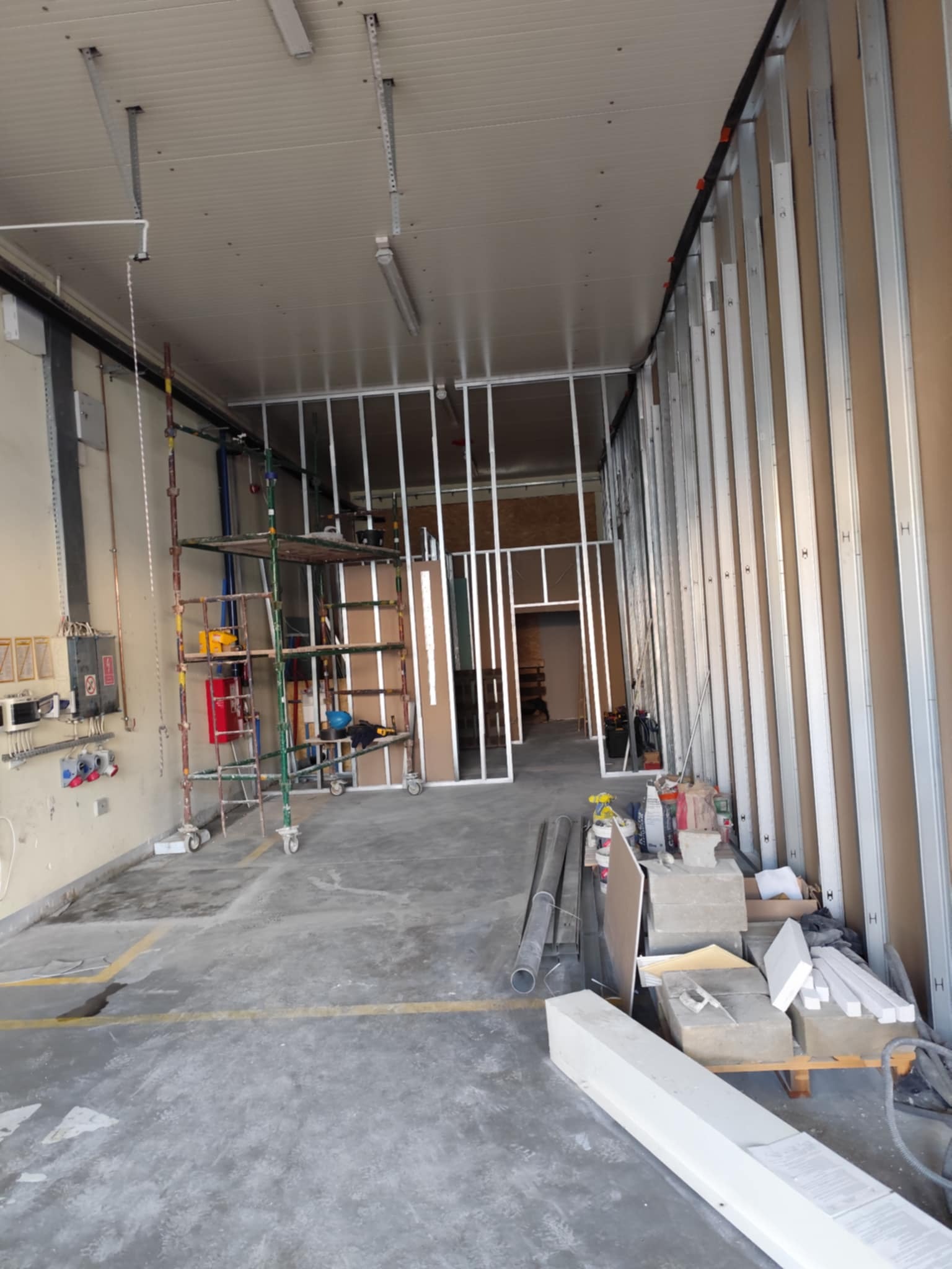 Wnętrze w trakcie prac z konstrukcją ścian z płyt karton-gips, widoczne profile, rusztowania i materiały budowlane. Stan surowy, przygotowanie do dalszych prac wykończeniowych.