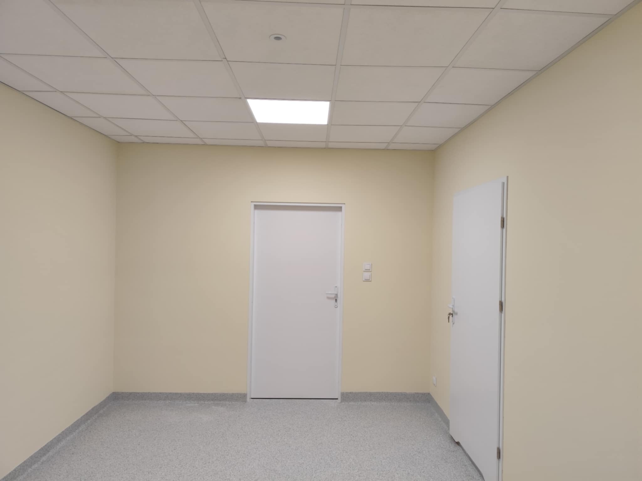 Wnętrze po remoncie w Poninie: ściany w odcieniach beżu, podwieszany sufit z oświetleniem i dwie białe, zamontowane drzwi. Widok na odnowione pomieszczenie.