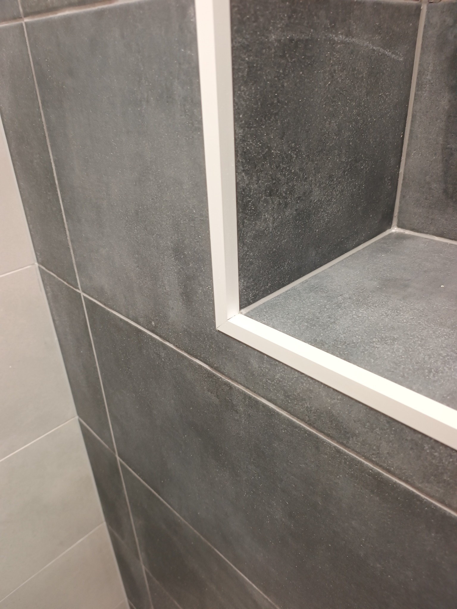 Szare płytki ścienne z białą listwą wykończeniową tworzące wnękę. Minimalistyczny design, precyzyjne ułożenie płytek i estetyczne wykończenie.