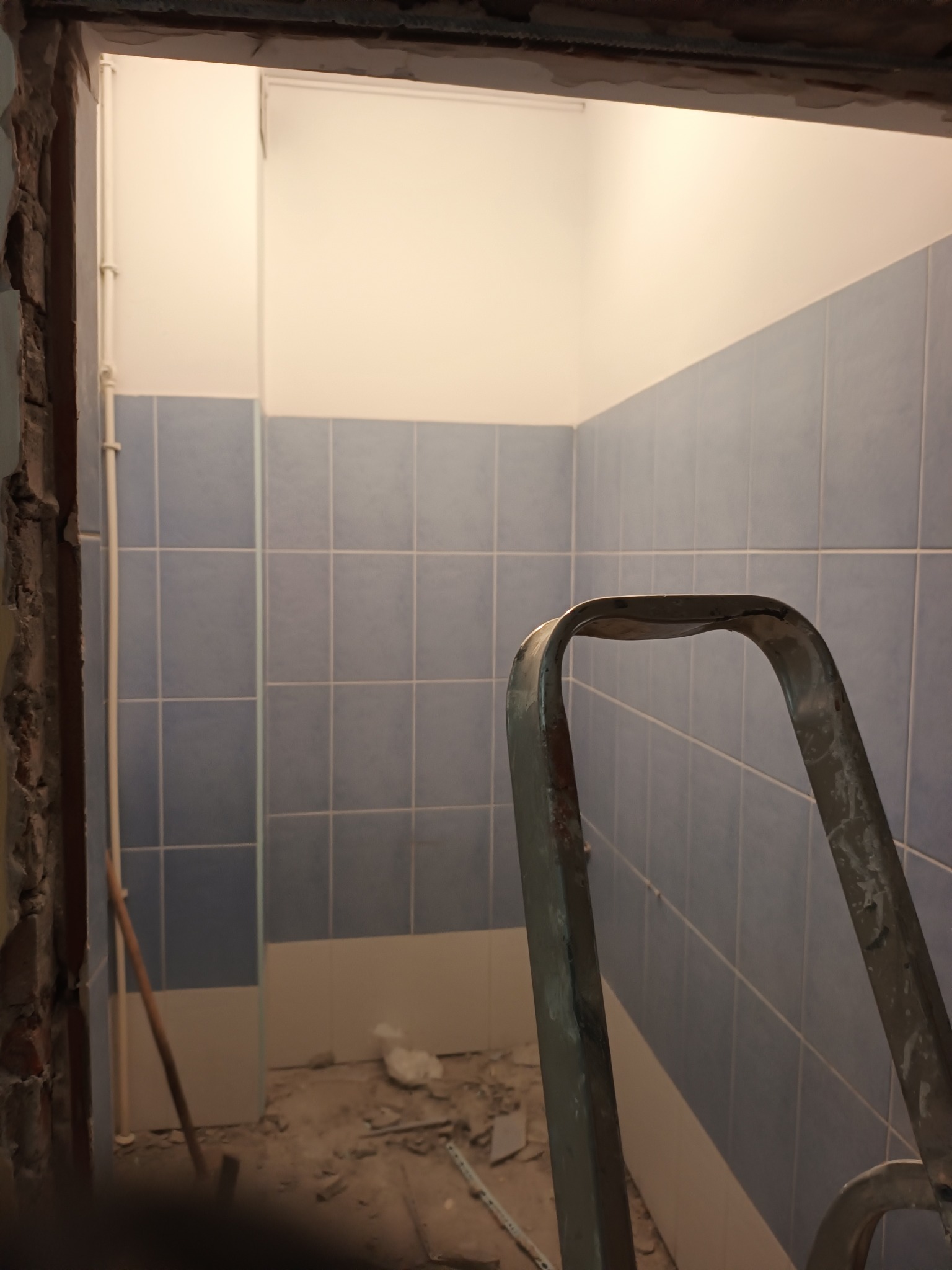 Łazienka w trakcie prac: niebieskie płytki na ścianach, widoczny fragment drabiny i gruz na podłodze. Świeżo położone płytki kontrastują z surowym stanem otoczenia.
